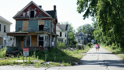 The image depicts a oncevibrant neighborhood now overshadowed by the presence of multiple abandoned and neglected properties In the foreground a house with peeling paint and boardedup windows stands out surrounded by overgrown grass and scattered deb