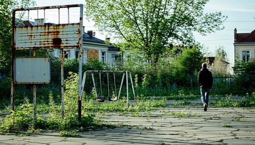The image depicts a oncevibrant neighborhood park now overgrown and neglected Weeds sprout through cracked pavement where children once played and rusted swings hang eerily still A faded sign at the entrance barely legible hints at the parks former g-3