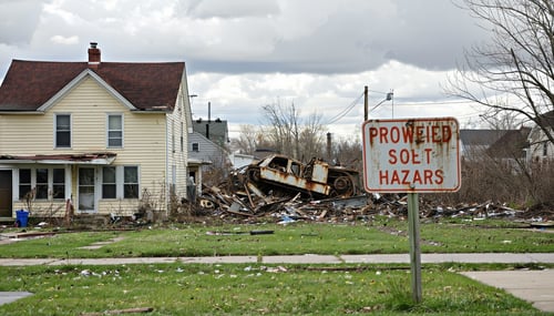 The image depicts a suburban neighborhood with a clear view of a derelict brownfield site in the background The foreground shows a modest singlefamily home with a neatly maintained lawn but its charm is overshadowed by the visible signs of neglect fr