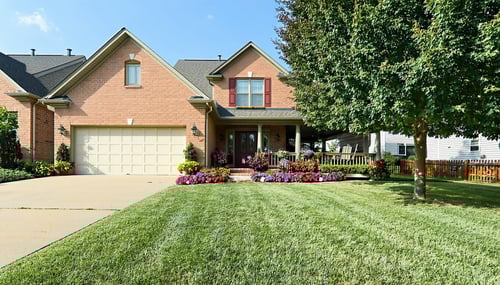The image depicts a wellmaintained suburban home in Fulton County showcasing its prominent physical characteristics The house constructed of warmbrick material features a welcoming front porch adorned with potted plants To the left a neatly manicured