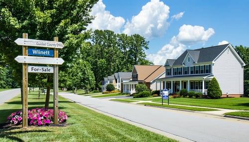 The image features a tranquil suburban street in Gwinnett County lined with neatly maintained homes showcasing various architectural styles from charming ranchstyle to modern twostory houses Lush green lawns and colorful flower beds enhance the invit-1
